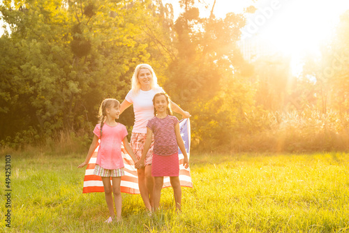Patriotic holiday. Happy family, mother and daughters with American flag outdoors on sunset. USA celebrate independence day 4th of July.
