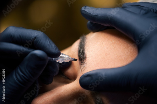 Microblading process by beauty master. Professional cosmetologist making permanent makeup on woman's eyebrow with tattoo pen machine.