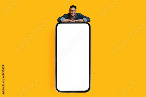 Handsome arab guy leaning on big smartphone with empty screen