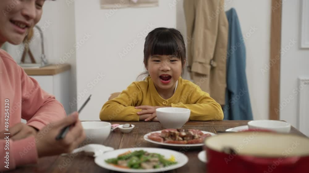 selective focus of happy Asian little girl asking her mother to refill her bowl. the woman sits down after putting a plate of vegetable on dining table at home selective focus of happy Asian little girl asking her mother to refill her bowl. the woman sits down after putting a plate of vegetable on dining table at home