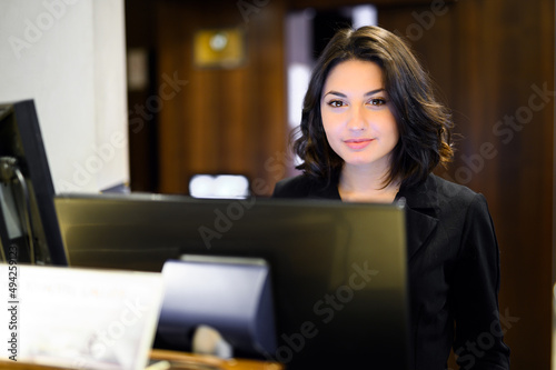 Happy female receptionist standing at hotel counter photo