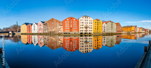 Wide panoramic view of old colorful wooden houses with reflections in river Nidelva in the Brygge district in Trondheim, Norway