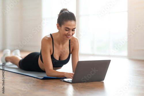 Young woman lying on yoga mat using laptop