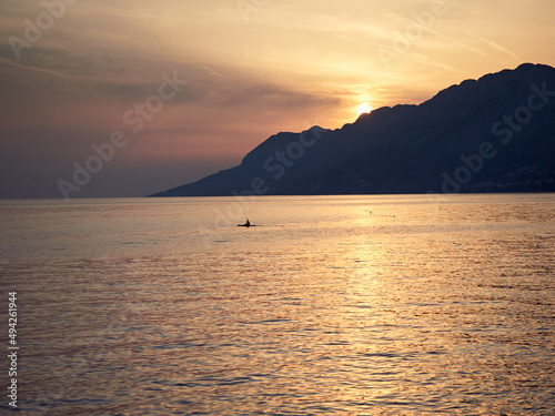 The sun is setting behind the Biokovo mountains on the Adriatic Sea in the Croatian town of Brela. Canoeist in the sea. A beautiful landscape.