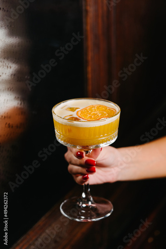 A woman's hand holds a cocktail in a bar. Alcoholic drink with orange