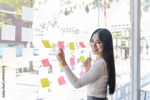 Young business leaders, beautiful women working in marketing, grow in statistics, reports, graphs, financial documents, using post-it notes in glass walls to write business plans