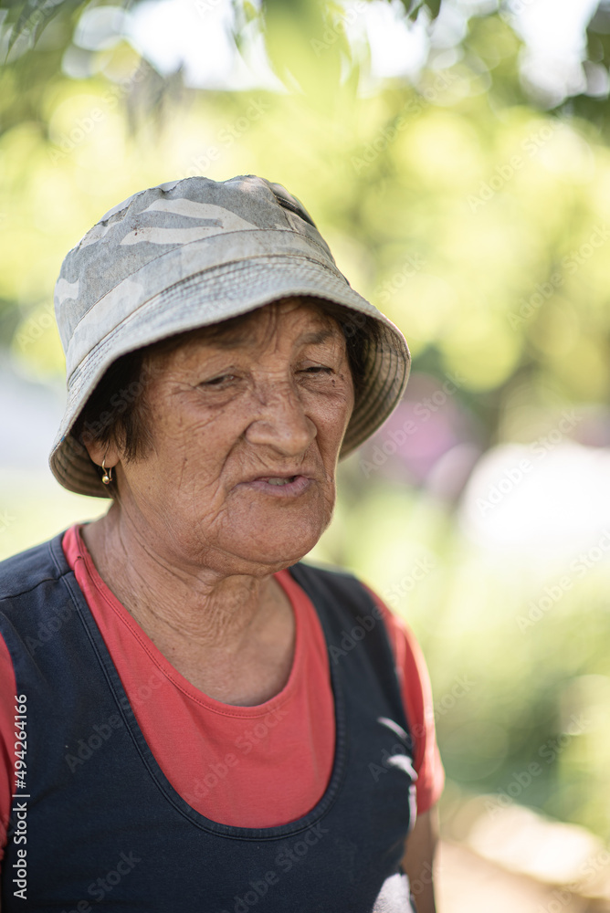 Close-up portrait of a pensive elderly woman in a panama hat in a summer garden.
