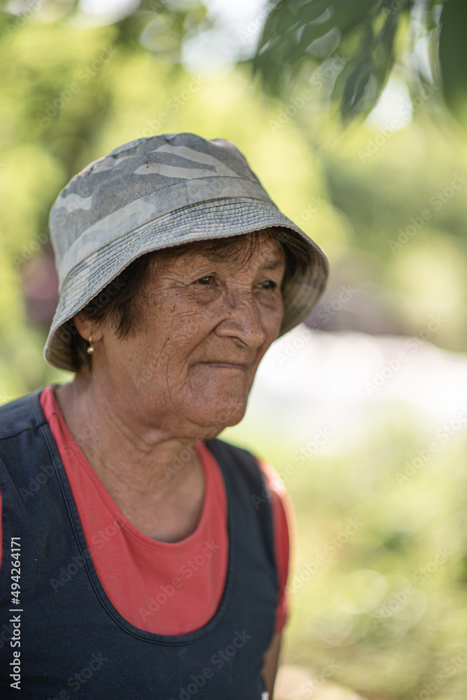 Close-up portrait of a pensive elderly woman in a panama hat in a summer garden.