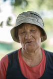 Close-up portrait of a pensive elderly woman in a panama hat in a summer garden.