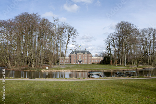 Winter barren trees on a sunny day with park and moat in the foreground and exterior facade of Slot Zeist castle in the background against a blue sky