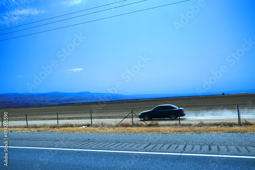 Lines separating mountains, hills, dried grass, farm land, and orchards beside highway 99 with wire fence under the blue sky