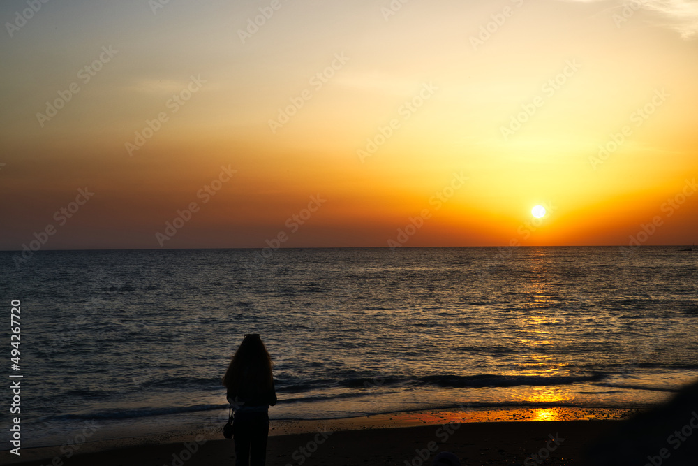 young girl standing on the beach watching the sunset