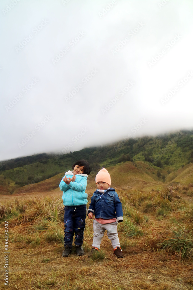 Fototapeta premium two asian toddler show their action standing on the mountain using their jacket