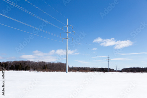 Low angle view of power line towers in field of snow seen during a sunny late winter day, Quebec City, Quebec, Canada