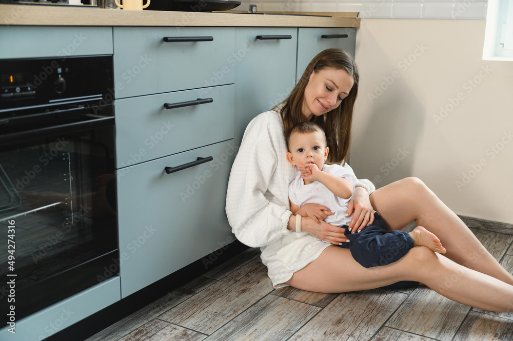 Happy mom and cheerful baby in the kitchen. Mother's love. Motherhood. The child is restless. Happy mom and cheerful baby in the kitchen. Mother's love. Motherhood. The child is restless.
