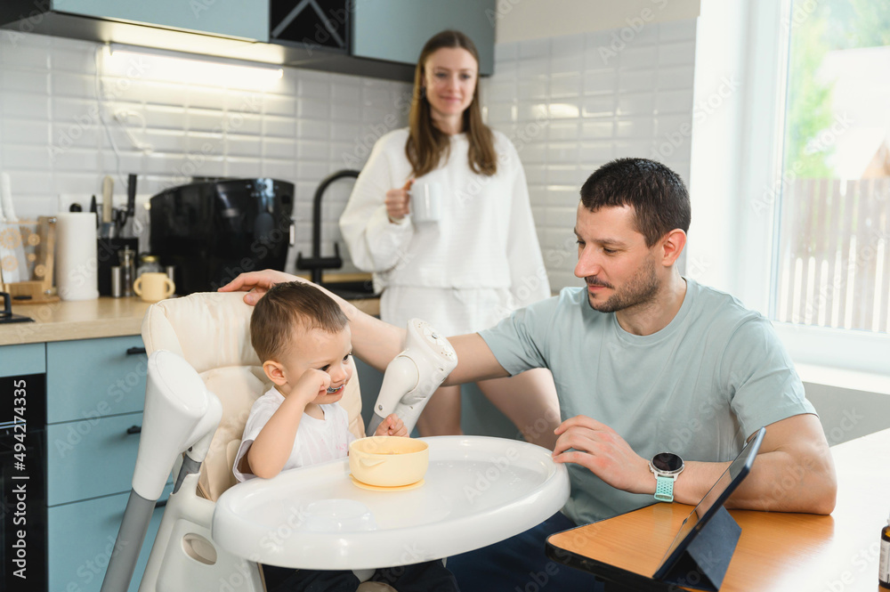 Young parents father and mother feeding the baby. Child on a highchair in the kitchen. Dad, mom and baby - happy full family