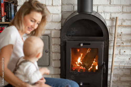 Defocused blonde mother and child hugs nearby fireplace. Family fireplace advertisement. Family spending time together © Татьяна Волкова