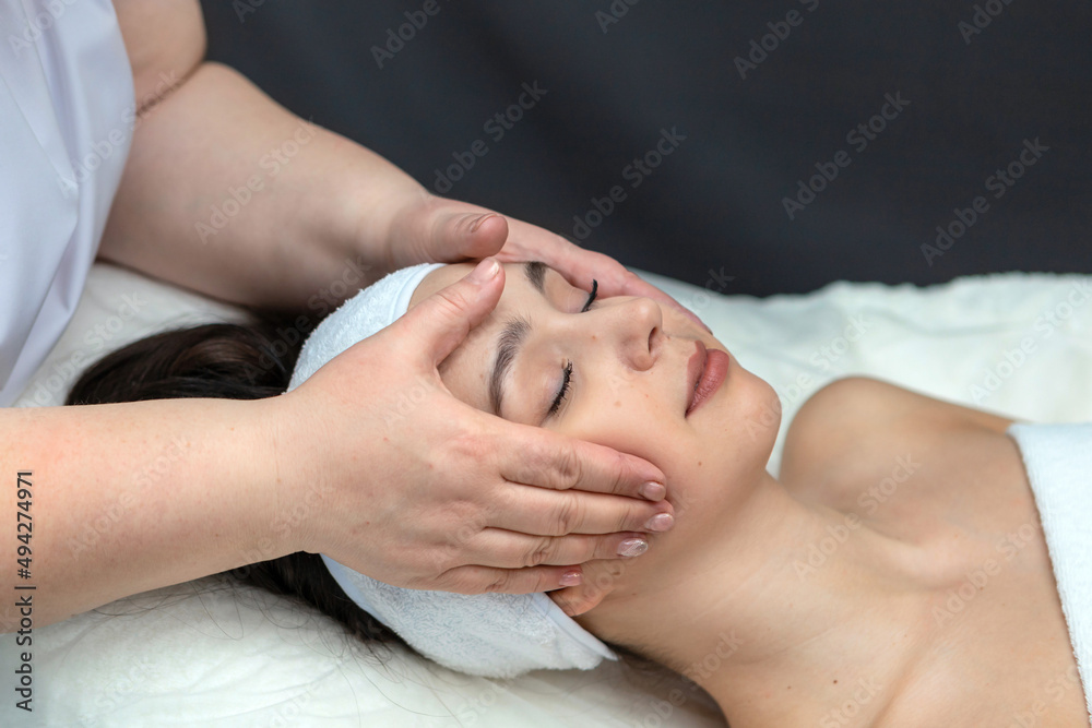 A girl's face in close-up during a facial treatment at a cosmetologist.The cosmetologist gives the client a facial massage.The concept of professional cosmetology.A young woman enjoys a facial massage