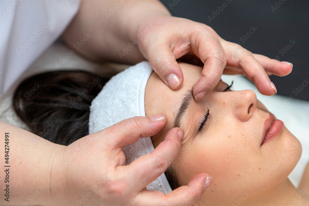 A girl's face in close-up during a facial treatment at a cosmetologist.The cosmetologist gives the client a facial massage.The concept of professional cosmetology.A young woman enjoys a facial massage A girl's face in close-up during a facial treatment at a cosmetologist.The cosmetologist gives the client a facial massage.The concept of professional cosmetology.A young woman enjoys a facial massage