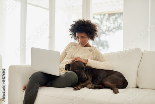 Hes such a good boy. Shot of an attractive young woman petting her dog while using her laptop on the sofa at home.