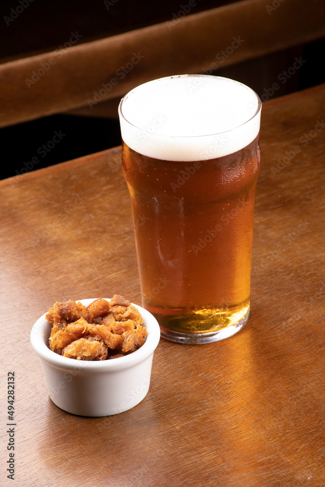 Craft beer pint with pork rinds on wooden table Craft beer pint with pork rinds on wooden table
