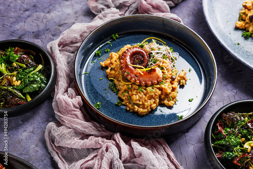 Fototapeta Naklejka Na Ścianę i Meble -  A portion of risotto with octopus tentacles. purple background. Top view