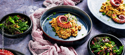 Fototapeta Naklejka Na Ścianę i Meble -  A portion of risotto with octopus tentacles. purple background. Top view
