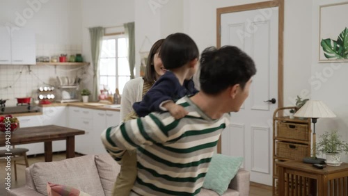 slow motion of cute Asian boy playing on his dad’s back at home. the man running away from the mother as she is reaching her hand to touch the boy