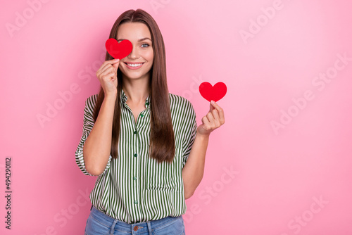 Photo of cheerful lady cover eye red heart beaming smile wear striped green shirt isolated pink color background