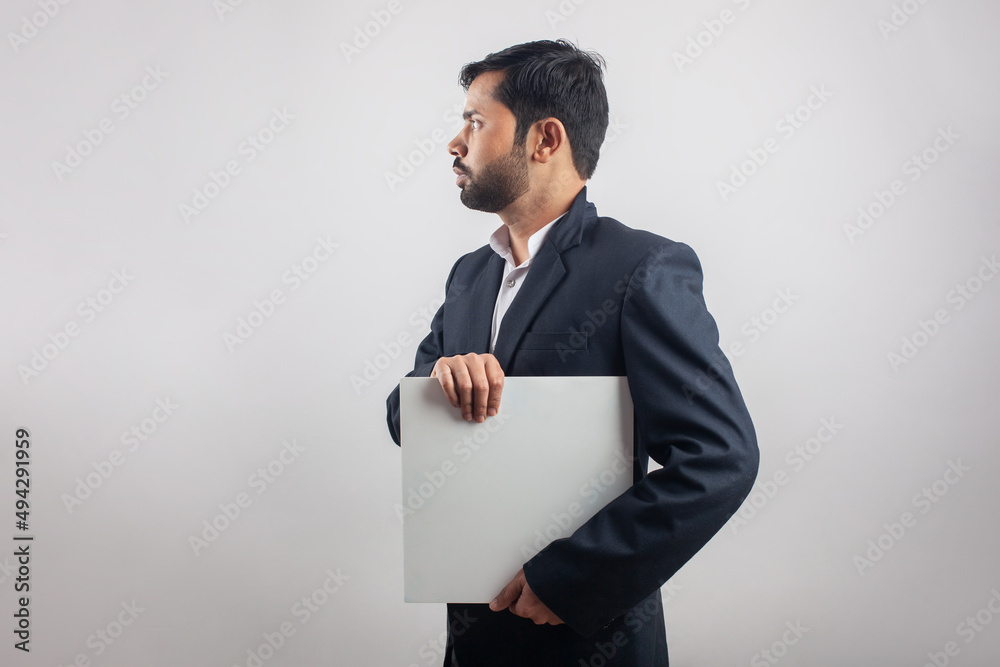 suit man holding a blank white billboard looking side view in grey background suit man holding a blank white billboard looking side view in grey background