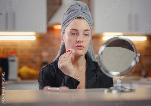 young woman looks in mirror using facial gua sha jade board at home. Lifting, skincare and lymphatic drainage of skin concept. Sculpting, lifting and anti-aging care. Skin care and beauty at home.