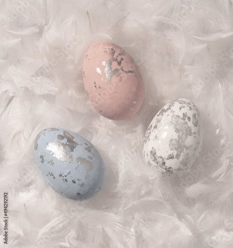 Blue, White and Pink Eggs with Black Spots Lying in a White Feathers. Modern Easter Holiday Composition with Small Eggs on a White Background ideal for Banner, Card, Greetings. Top-Down View. No text.
