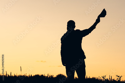 silhouette of a man on the background of a sunset waving his hand in greeting, a cap in his hand