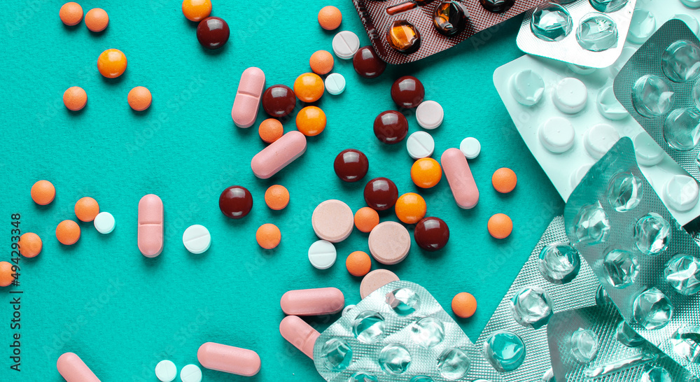 A lot of tablets on a turquoise background . probiotic capsule and antibiotic tablet