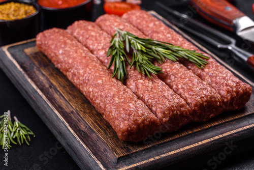 Fresh raw mince for grilled kebab with spices and herbs on a dark concrete background