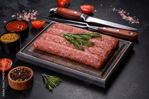 Fresh raw mince for grilled kebab with spices and herbs on a dark concrete background