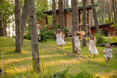 Group of happy preteen girls running among trees on green lawn in country estate