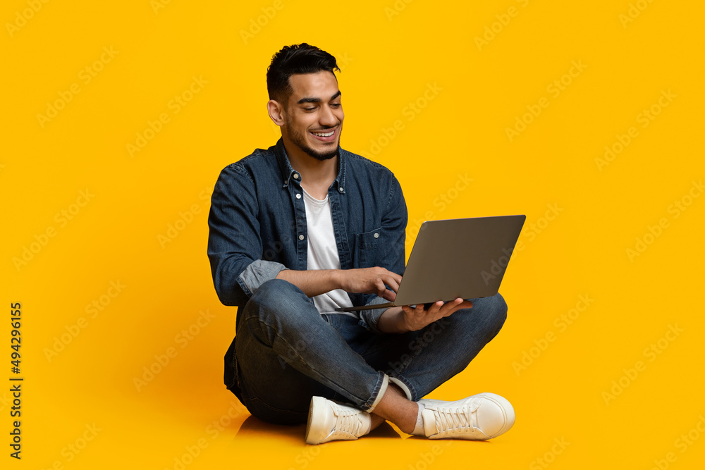 Happy middle eastern guy using modern notebook, isolated on yellow