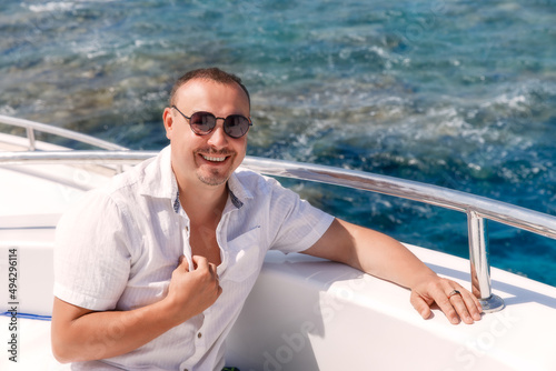 Portrait of adult man sitting on a yacht and looking at camera and wearing white shirt. Relaxing in summer during the trip. 