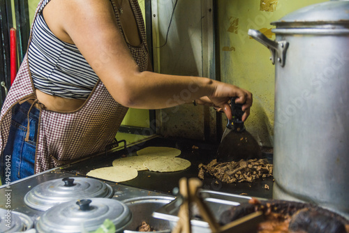 Mexican taquera woman prepares meat and chorizo tacos on the comal at her street stall. photo