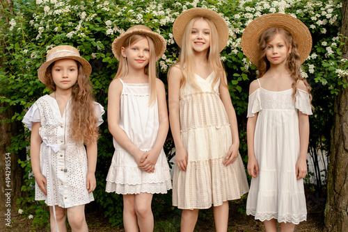Obraz na plátne Smiling tween girls standing in summer park near green blooming bush