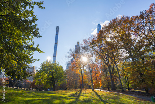 The sun illuminates autumnal leaf color trees in Central Park from among the Ultra-luxury high-rise residential skyscraper in Billionaires’s Row on November 2021 at New York City NY USA.