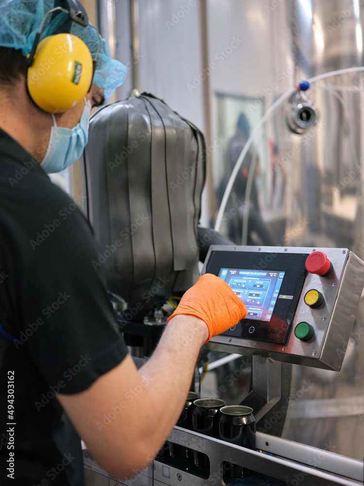 Worker with mask working with an electronic machine in a craft beer factory