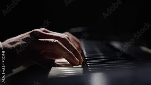 Male hands touch piano keys and play fast jazz melody. Pianist plays chords creating music on piano in dark. Keys of musical instrument. Musician's fingers close up. Slow motion ready at 59.94fps.