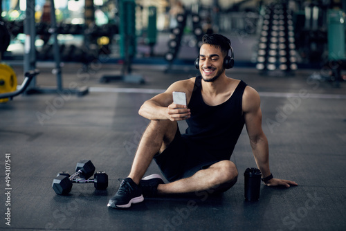 Fitness Application. Smiling Middle Eastern Sportsman Using Smartphone At Gym
