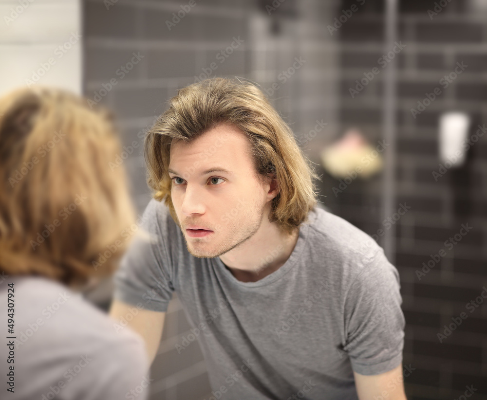 Fototapeta premium young man looking in the mirror,combing his hair,looking at problems on face.