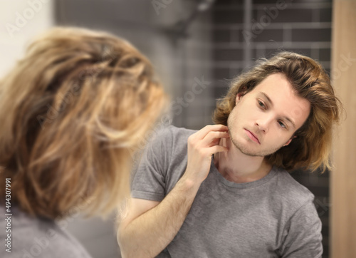 young man looking in the mirror,combing his hair,looking at problems on face.