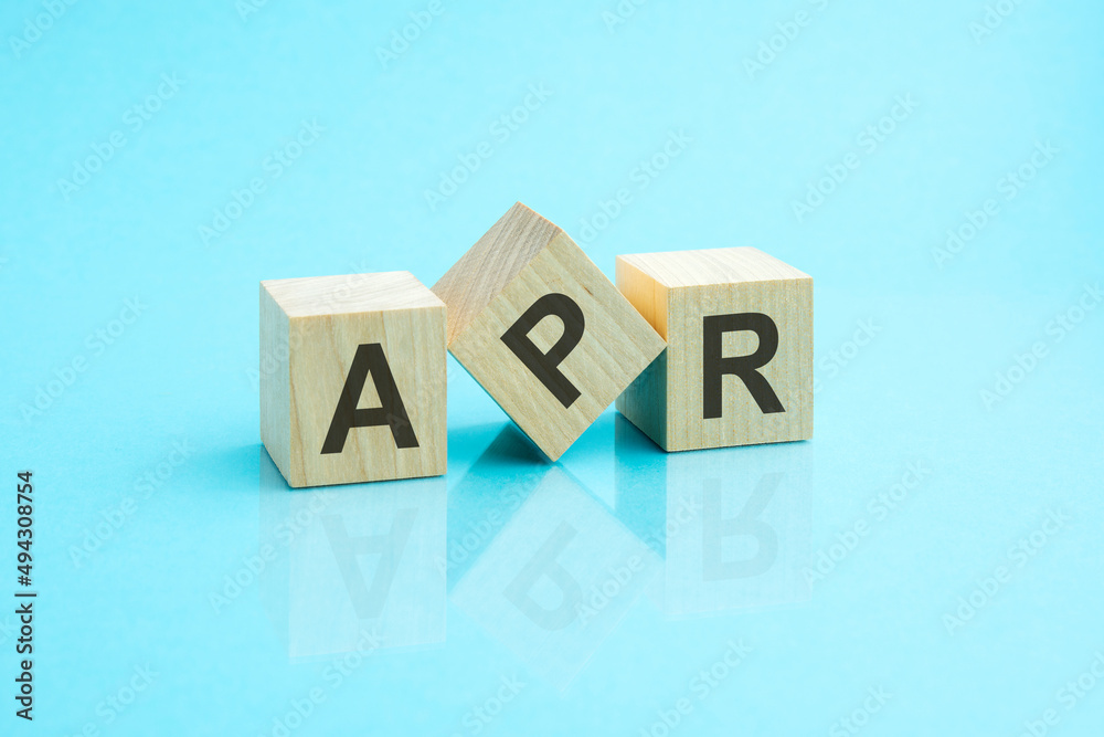 three wooden cubes with the letters APR on the bright surface of a blue table three wooden cubes with the letters APR on the bright surface of a blue table