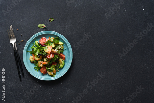 Mix salad with tomatoes and shrimp with pesto sauce on a black background. View from above