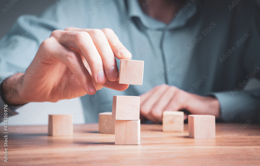 The man's hand adds a wooden block in place. Business success concept. The man's hand adds a wooden block in place. Business success concept.